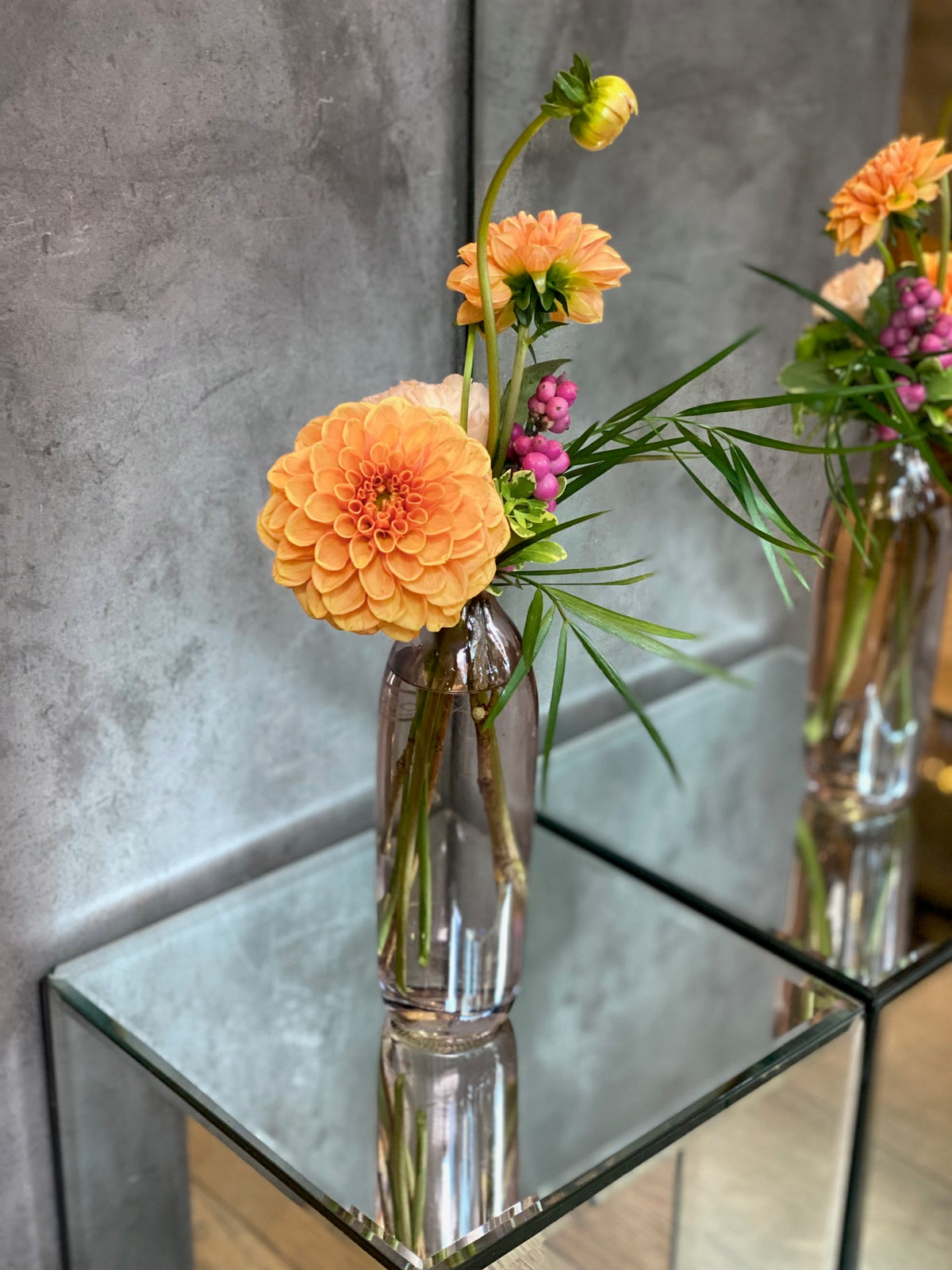 Set of three glass bud vases with seasonal flowers and greenery in warm autumn tones.