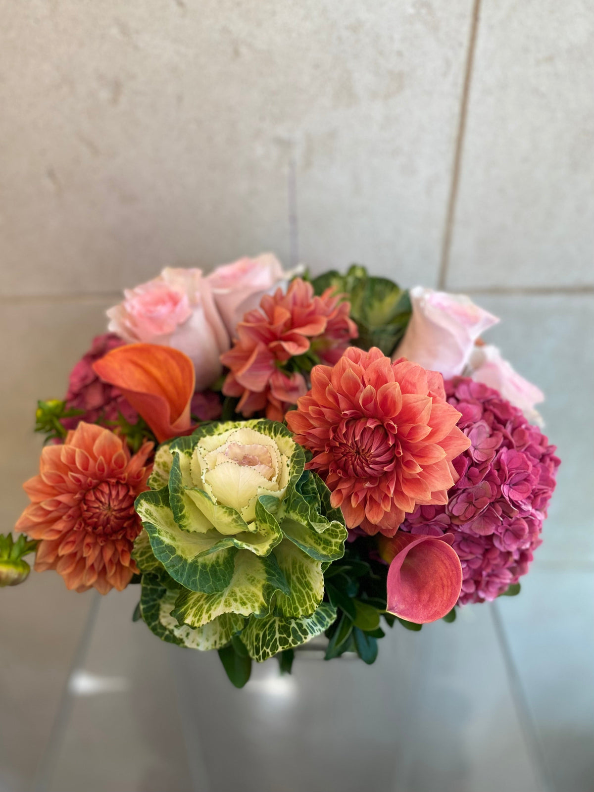Autumn floral arrangement with dahlias, hydrangeas, calla lilies, and ornamental kale in warm pink and coral tones.
