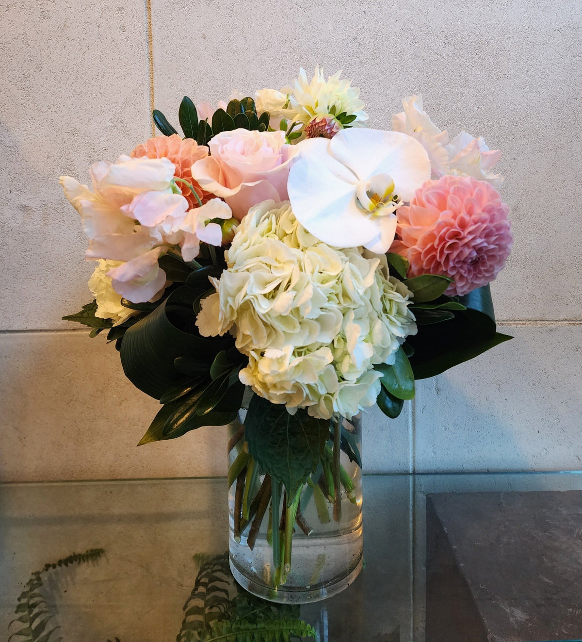 Blush and white floral arrangement with hydrangeas, roses, dahlias and white Phalaenopsis orchids in a clear glass vase.