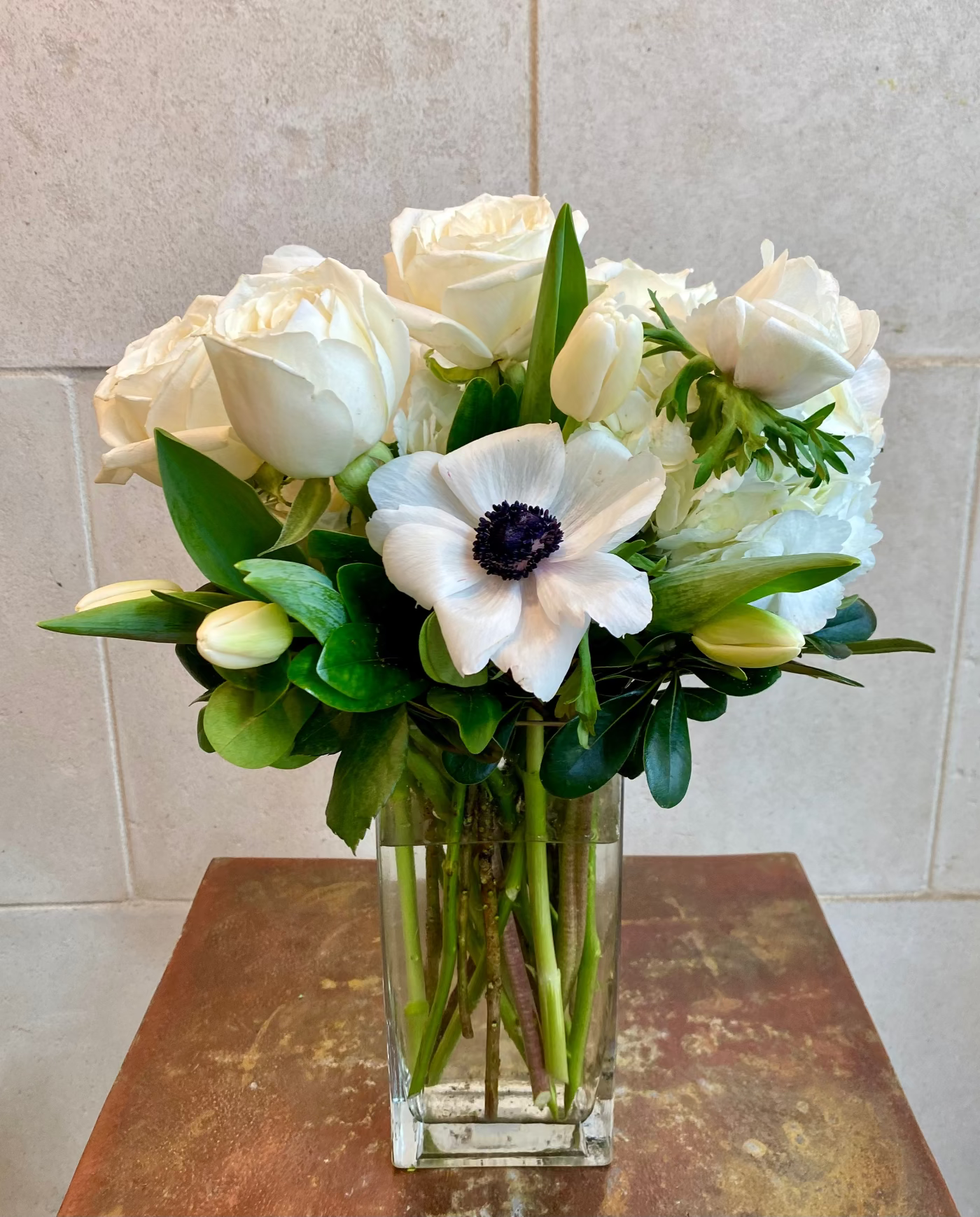 All-white floral arrangement with seasonal blooms in a clear glass vase.
