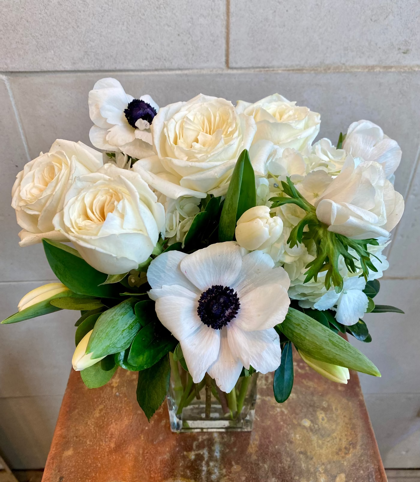 All-white floral arrangement with seasonal blooms in a clear glass vase.