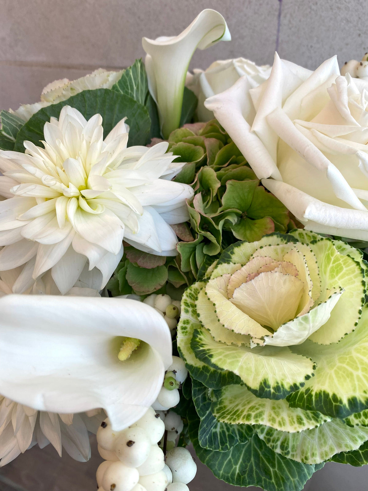 White and green floral arrangement with hydrangeas, roses, dahlias, ornamental kale, and seasonal foliage.