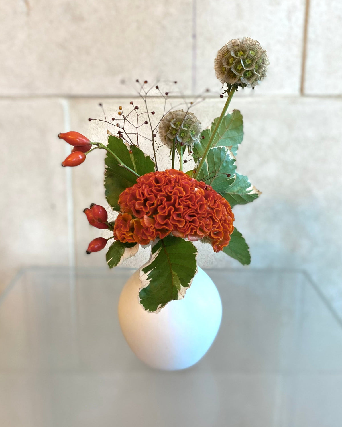 Set of three white ceramic bud vases with seasonal flowers in warm orange and coral tones