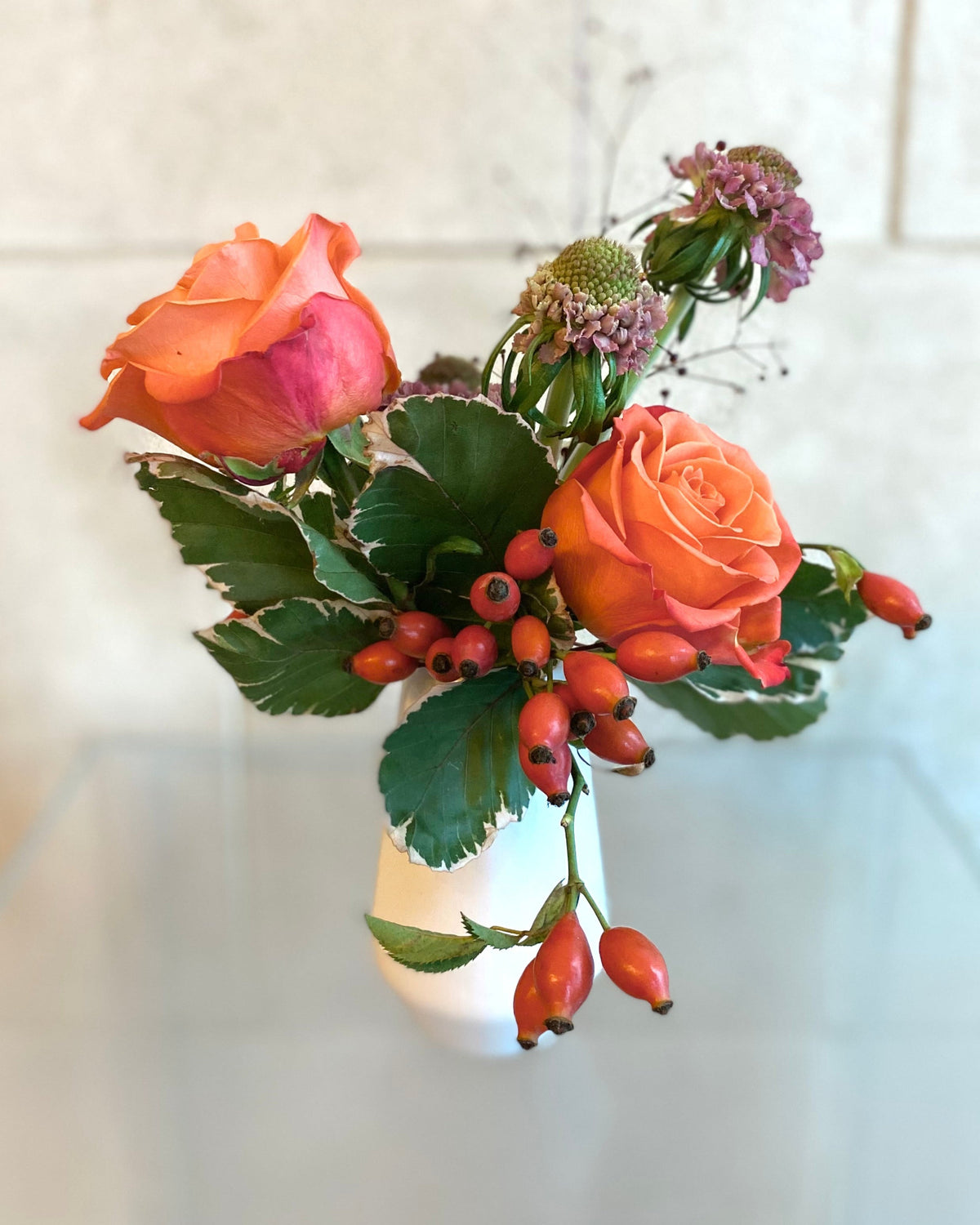 Set of three white ceramic bud vases with seasonal flowers in warm orange and coral tones