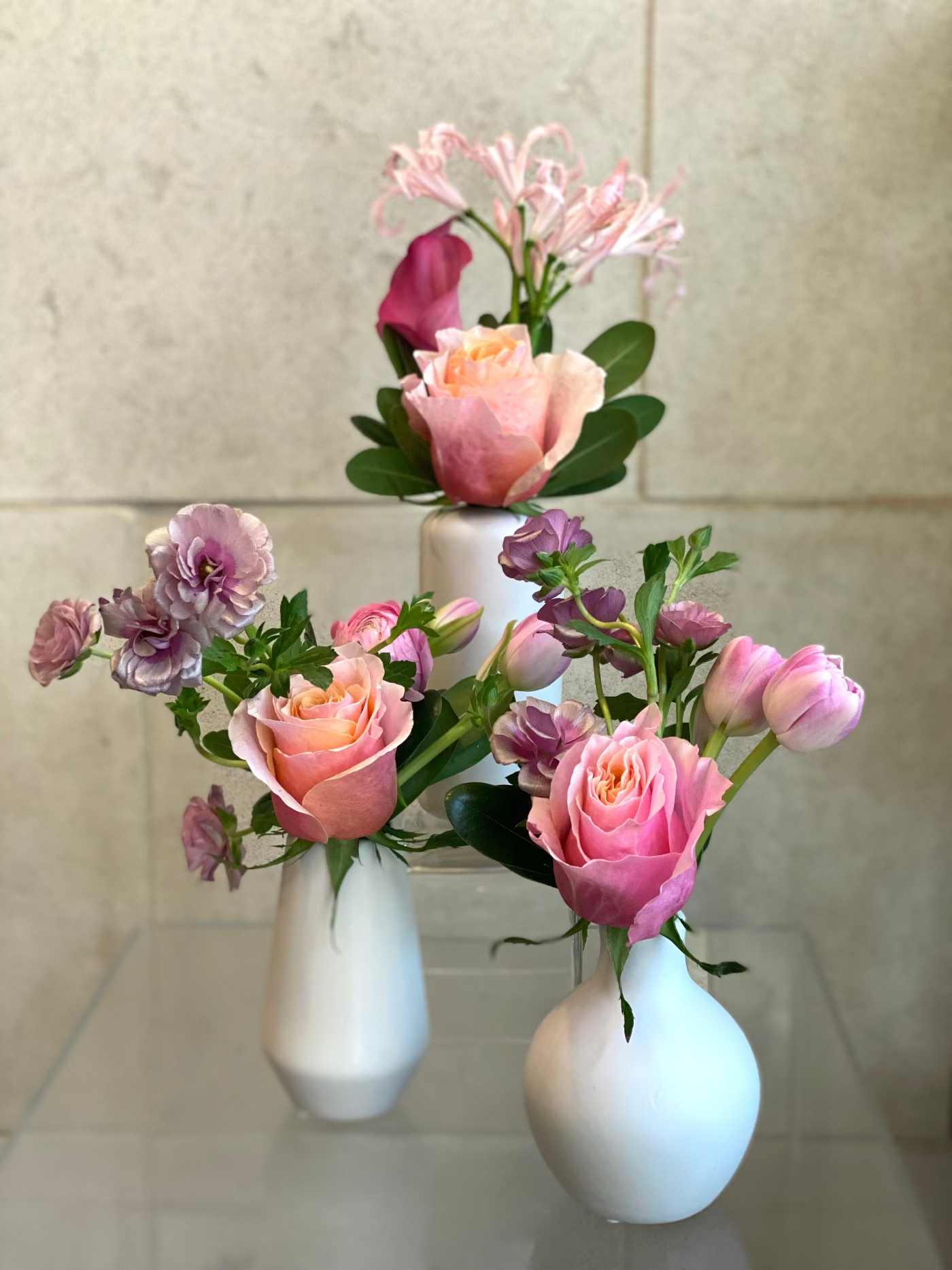 Set of three white ceramic bud vases with seasonal flowers in soft pink and lavender tones
