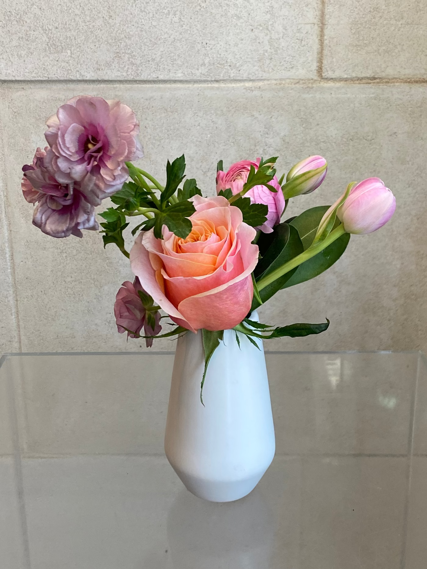 Set of three white ceramic bud vases with seasonal flowers in soft pink and lavender tones.