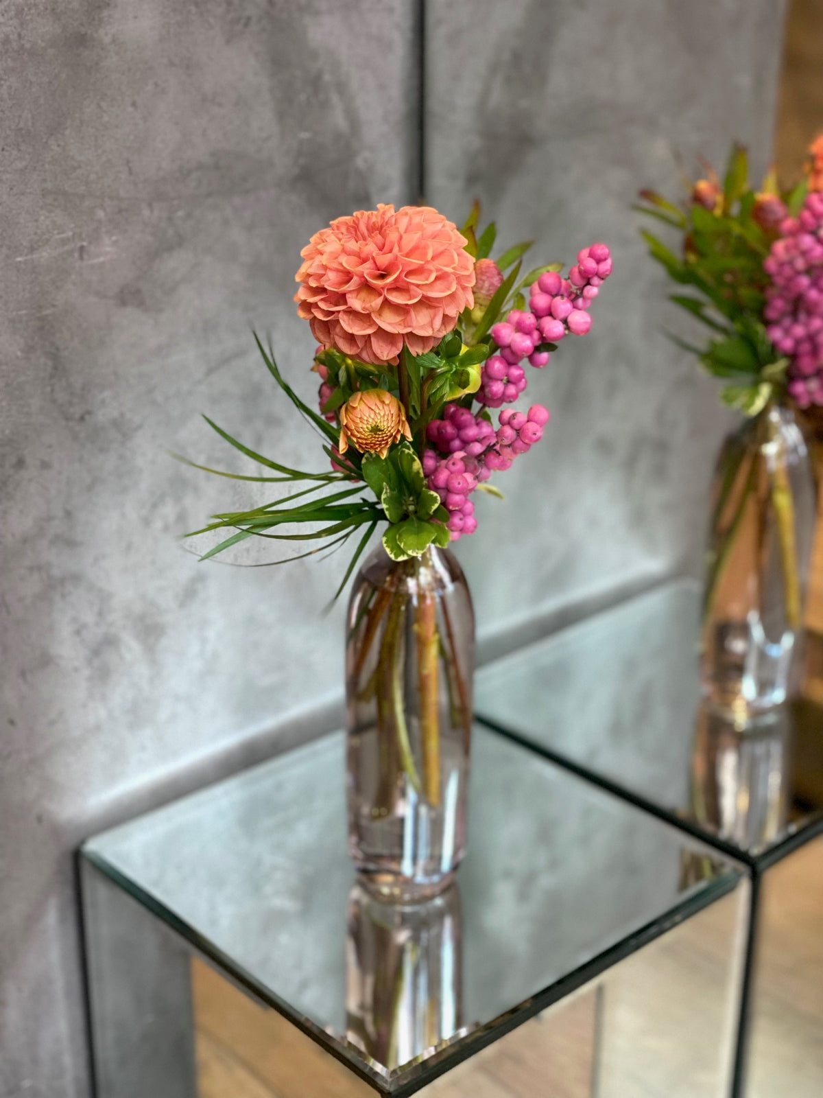 Set of three glass bud vases with seasonal flowers and greenery in warm autumn tones.