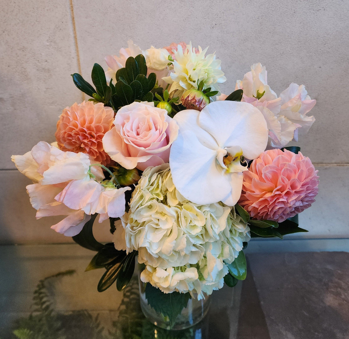 Blush and white floral arrangement with hydrangeas, roses, dahlias and white Phalaenopsis orchids in a clear glass vase.
