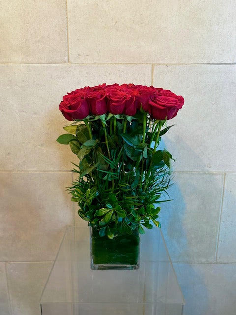 Red Freedom roses arranged in a leaf-lined glass cube vase with fresh greenery.