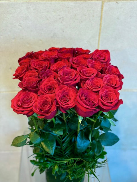 Red Freedom roses arranged in a leaf-lined glass cube vase with fresh greenery.