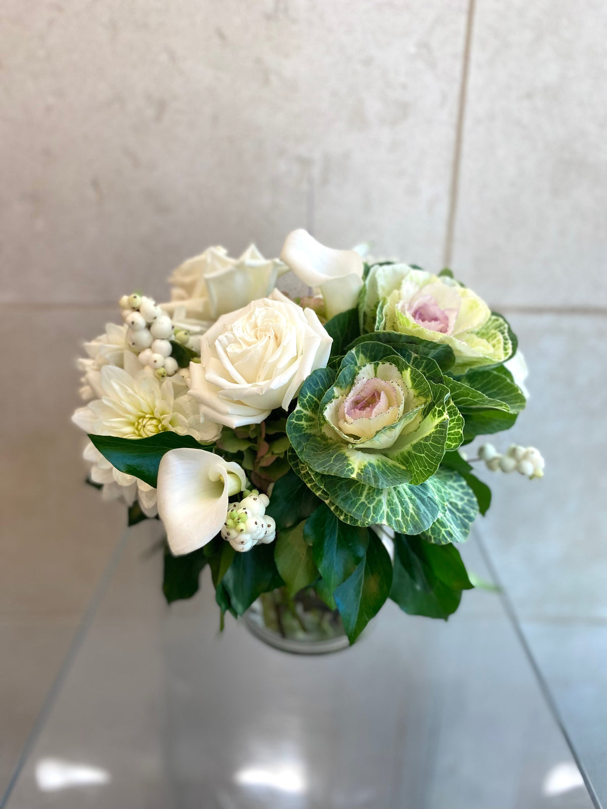 White and green floral arrangement with hydrangeas, roses, dahlias, ornamental kale, and seasonal foliage.