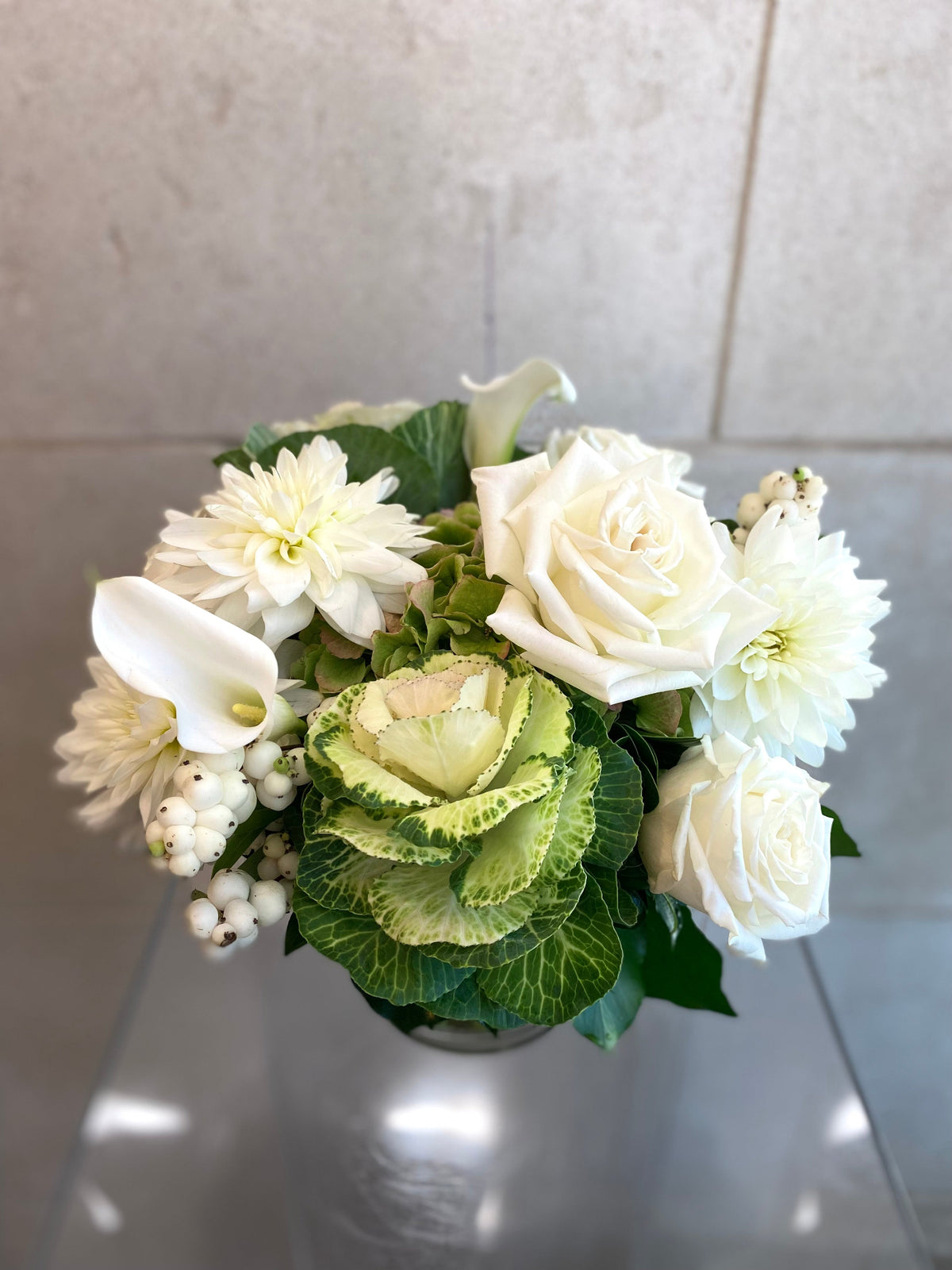 White and green floral arrangement with hydrangeas, roses, dahlias, ornamental kale, and seasonal foliage.