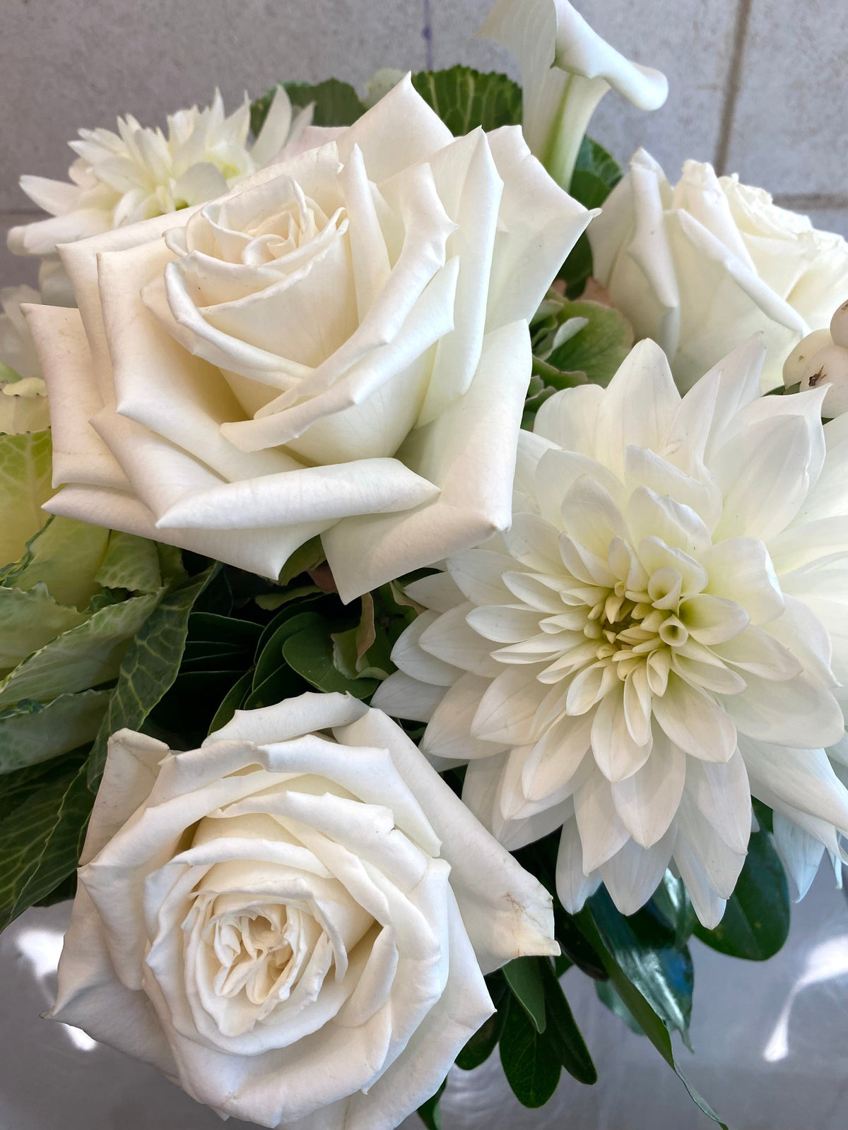 White and green floral arrangement with hydrangeas, roses, dahlias, ornamental kale, and seasonal foliage.