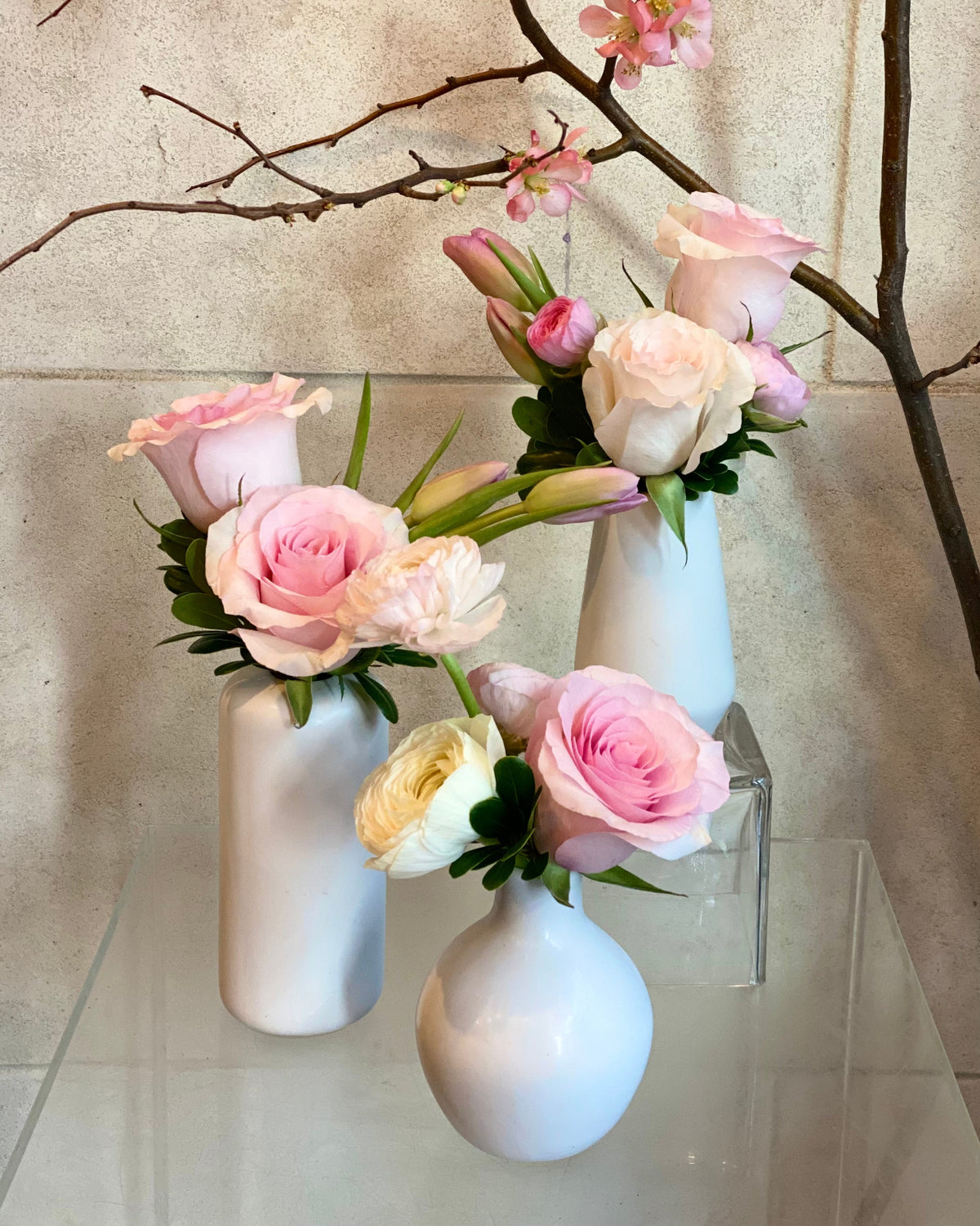 Set of three white ceramic bud vases with seasonal flowers in blush pink and cream tones
