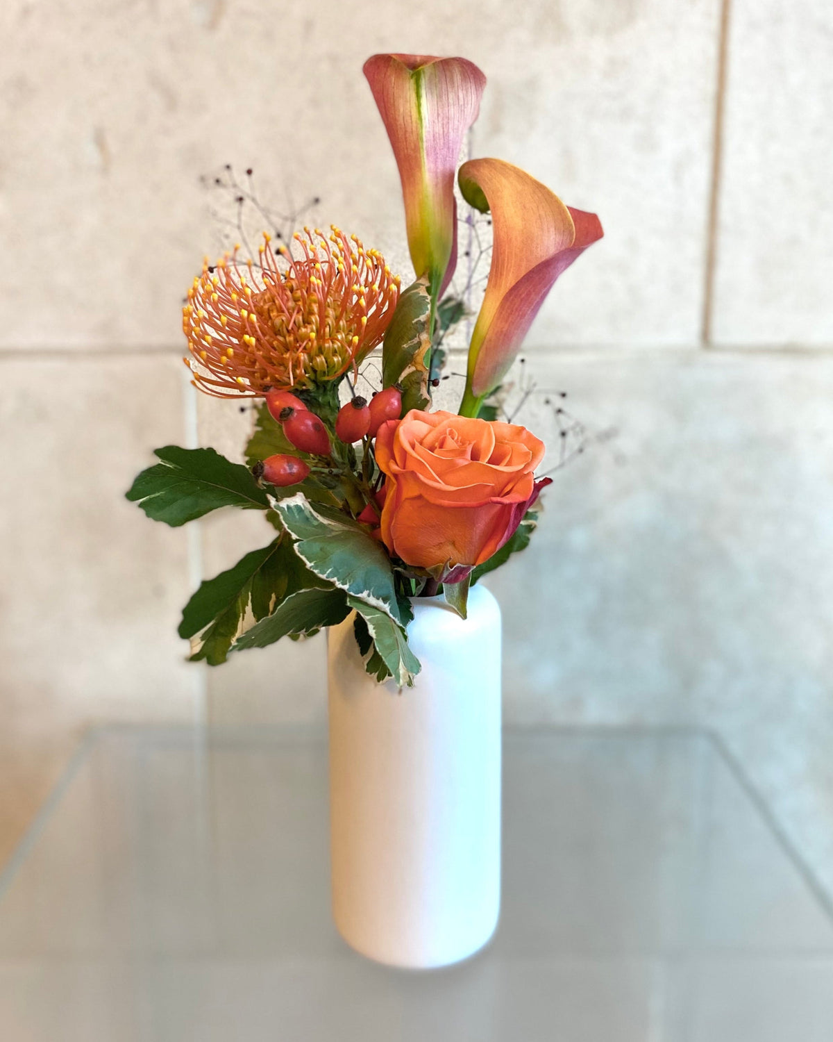 Set of three white ceramic bud vases with seasonal flowers in warm orange and coral tones