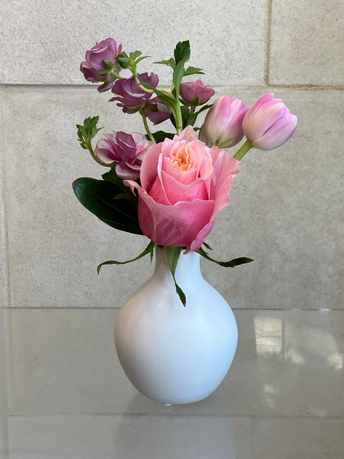 Set of three white ceramic bud vases with seasonal flowers in soft pink and lavender tones.