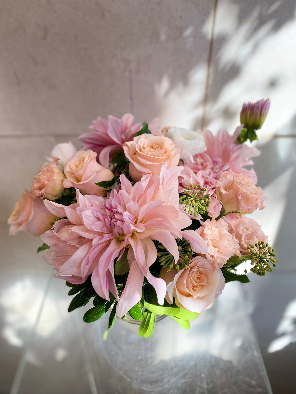 Soft pink floral arrangement with blush roses, pink dahlias, seasonal blooms, and fresh greenery.