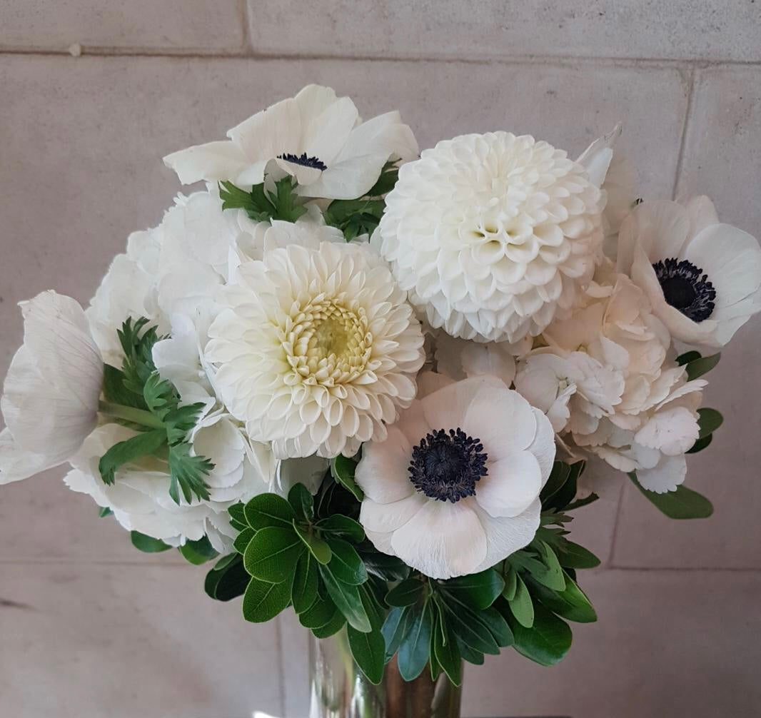 All-white floral arrangement with seasonal blooms in a clear glass vase.